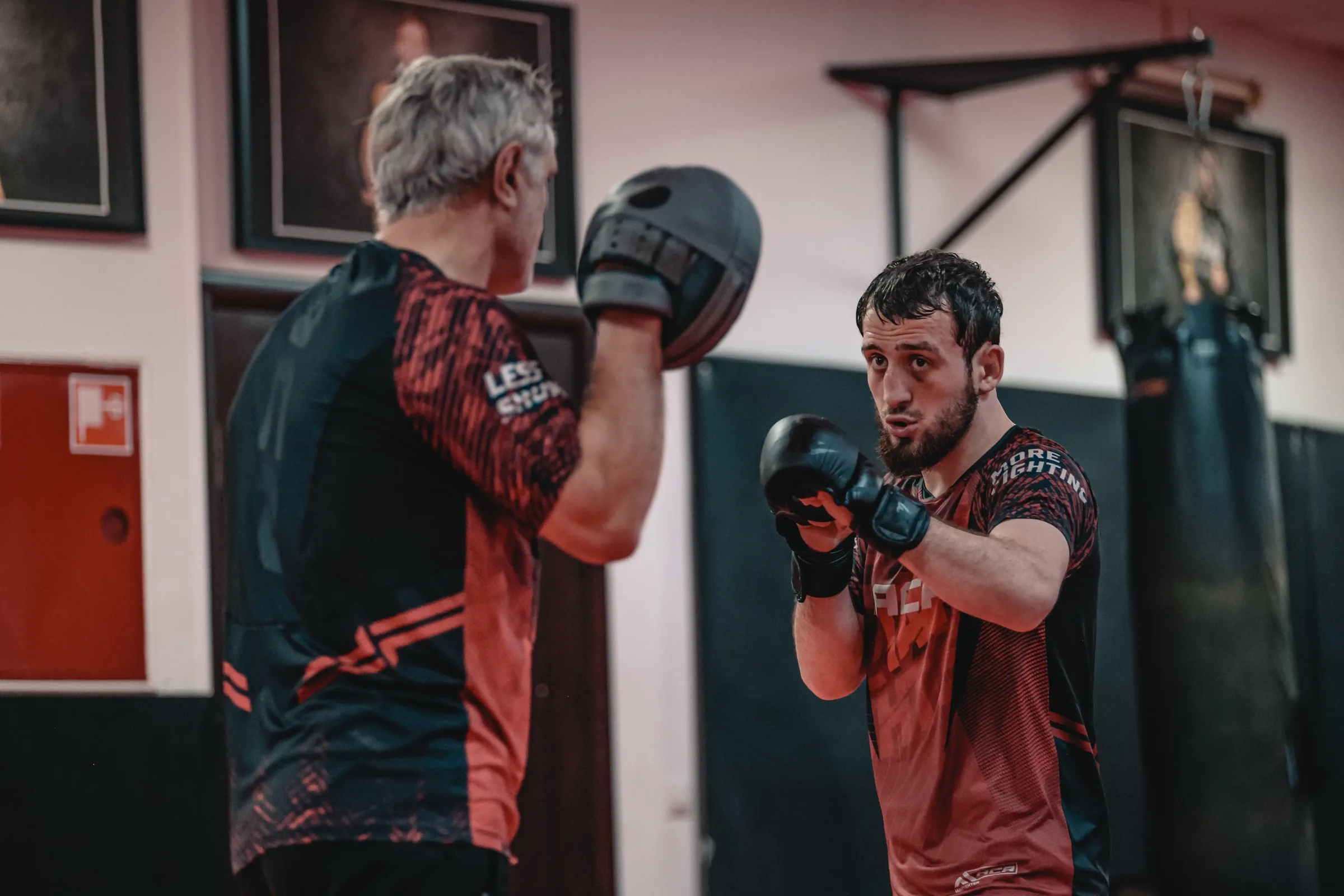 Intense face-to-face MMA sparring in a Grozny gym, red gloves, focused stares