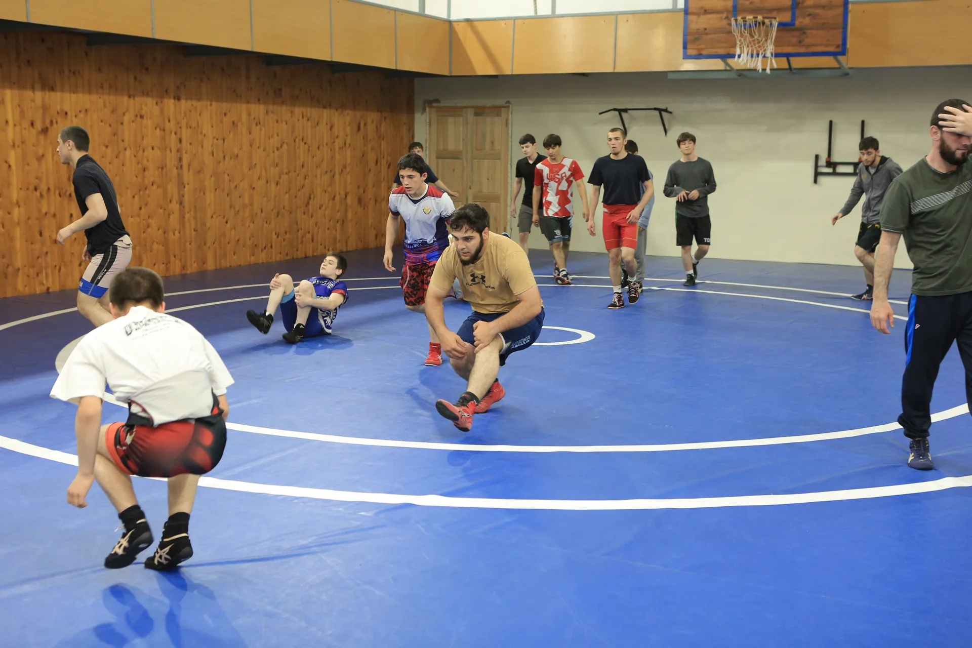 Wrestlers drilling sprawls in a line on the mat of the Dagestani room