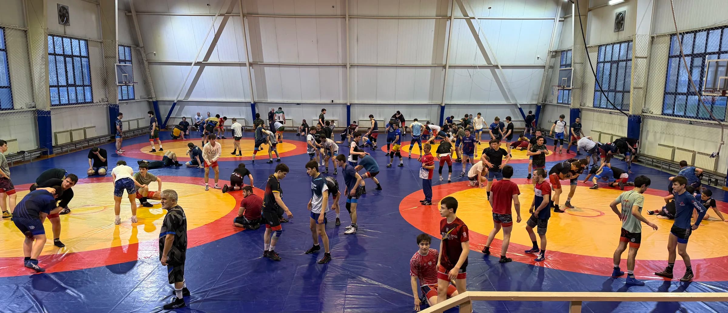 Overhead view of a wrestling hall in Dagestan: three competition mats filled with dozens of wrestlers training